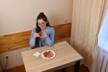 Bir kadın kahvaltıda çay içer ve hamur işi yer..