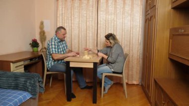 Oturma odasındaki masada oturan erkek ve kadın tahta bloklarla masa başı oyunu oynuyorlar, sürece odaklanıyorlar..