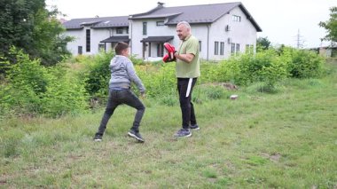 Çocuk, Green Park 'ta yetişkin koçuyla boks antrenmanı yapıyor..