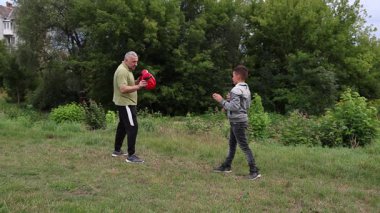 Çocuk, Green Park 'ta yetişkin koçuyla boks antrenmanı yapıyor..
