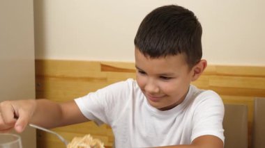 Bir çocuk masada otururken çatalla spagetti yer..