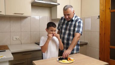 Bir adam ve bir çocuk mutfakta meyve yiyorlar..