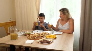 Bir kadın ve oğlu masada otururken meyve suyu içiyorlar..