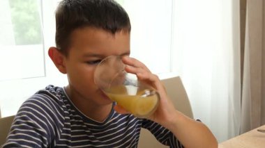 Çocuk masada otururken bardaktan meyve suyu içiyor. Yakın plan.