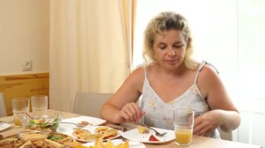 Bir kadın masada otururken bardaktan meyve suyu içer..