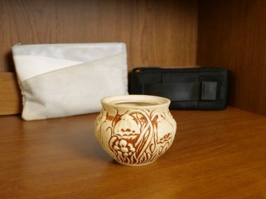 Tahta bir rafa oyulmuş çiçek süsüyle seramik kap.