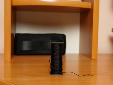 Ahşap yüzeyde duran siyah iplik makarası, yakın aksesuar dikiyor..