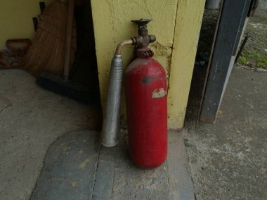 Eski kırmızı yangın söndürücü, metal silindirli, elektrik tesisatı alanında sarı bir duvarın yanında duruyor..