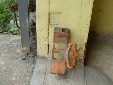 Beton zeminde sarı bir duvara yaslanmış paslı metal durdurucu ya da ayraç.