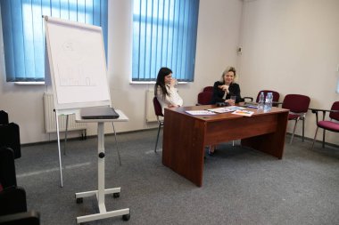 İki iş kadını büroda evrakları ve su ile masada oturuyorlar.