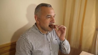 Yetişkin bir adam evde atıştırırken çikolata parçacıklı kurabiyeler yiyor.