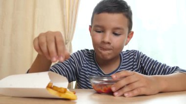 Çocuk evde yemek yerken ketçapla patates kızartması yiyor..