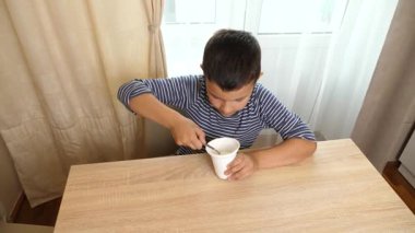 Çocuk gündüz vakti pencerenin yanındaki masada yoğurt ya da ekşi krema yiyor..