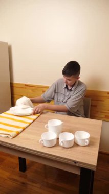 Genç bir çocuk, bir evde mutfakta bulaşıkları kurutuyor ve temizliyor. Kendi başına günlük ev işlerini yapıyor..