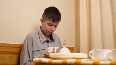 Genç bir çocuk, bir evde mutfakta bulaşıkları kurutuyor ve temizliyor. Kendi başına günlük ev işlerini yapıyor..