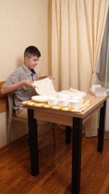 Genç bir çocuk, bir evde mutfakta bulaşıkları kurutuyor ve temizliyor. Kendi başına günlük ev işlerini yapıyor..