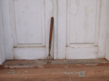 Tahta saplı eski bir bahçe yetiştiricisi beyaz kapıların yanında duruyor..