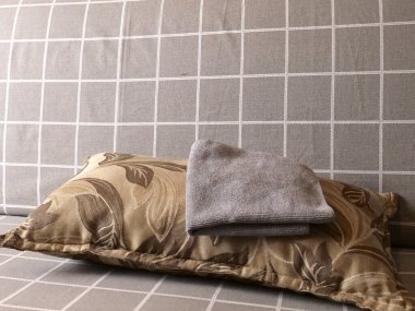 Dekoratif desenli yastık katlanmış gri havluyla kareli bir kanepede, duvarın yanında, iç mekanda rahat, durgun bir hayat.