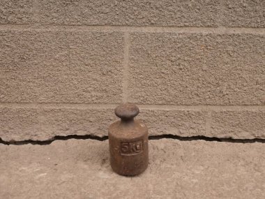 Eski dökme demir ağırlığı ile beton üzerinde duran kabataslak bir duvar arka planı.