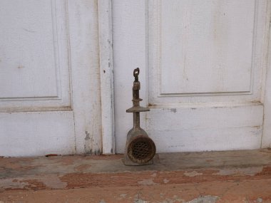 Eski el değirmeni ya da paslı kıyma makinesi beyaz ahşap kapıların yanında duruyor..