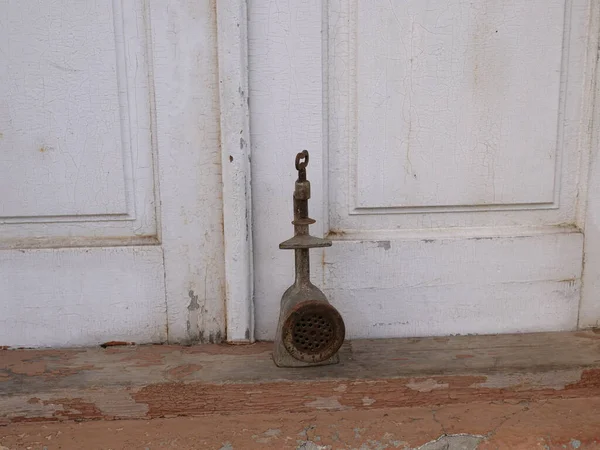Eski el değirmeni ya da paslı kıyma makinesi beyaz ahşap kapıların yanında duruyor..