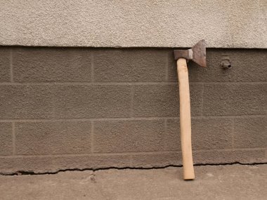 Ahşap saplı eski bir balta sert desenli beton bir duvara yaslanmış ve yere yakın bir çatlak var..