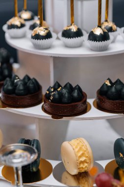 Siyah kremalı ve altın aksanlı çikolatalı pastalar çok katlı tatlı standında sergileniyor.