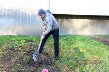 Apartman avlusunda bahçe işleriyle uğraşan bir adam kürekle toprağı eğip kazıyor.