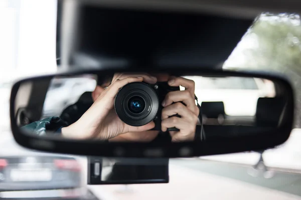 Homem segurando uma câmera senta-se no assento do motorista e olha no espelho retrovisor — Fotografia de Stock
