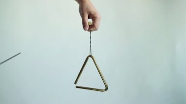 Eller müzikal bir üçgen çalar. Beyaz arka planda birkaç kez vurun