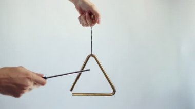 Eller müzikal bir üçgen çalar. Beyaz arka planda birkaç kez vurun