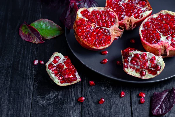 Büyük bir nar, parçalara bölünmüş. Karanlık bir arka planda. Tahıllar yakınlarda serpilmiş. Sonbahar konsepti. Vitaminler, sağlıklı yaşam tarzı. Boşluğu kopyala.