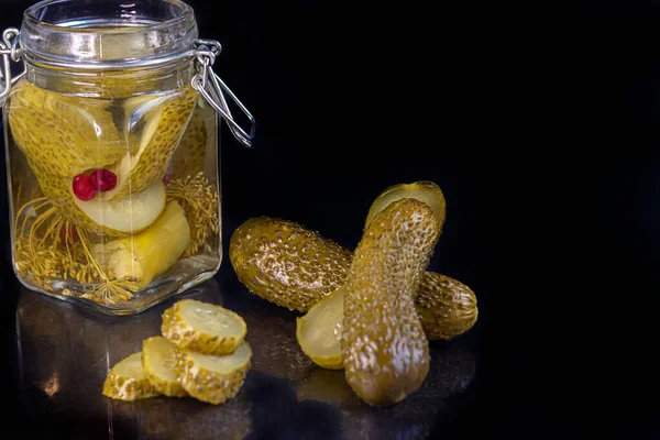 Pickled cucumbers in a glass jar and on a wooden board. Fermented food on a gray background. Copy space.