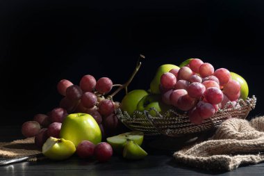 Koyu arkaplanda pembe üzümler ve yeşil elmalar. Durgun hayat. Vitamin sepeti. Boşluğu kopyala.