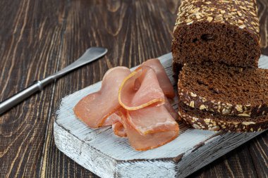 Çavdar ekmeğiyle füme et dilimlemek. Sandviç yapıyorum. Ahşap bir arka planda.