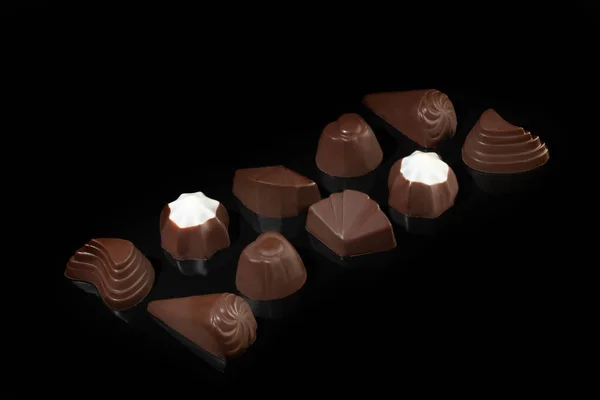 Chocolate candies on a dark background with reflection. Piece by piece and as a whole. Filling of nuts and fruits. — Stock Photo, Image