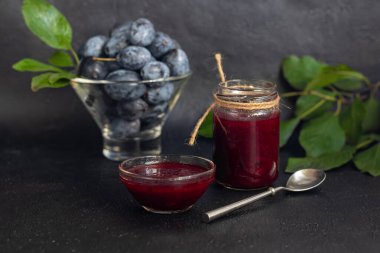 Kavanozda erik reçeli. Arka planda erikler var. Tkemali sosu. Kış için hazırlanıyorum. Karanlık arka plan. Boşluğu kopyala.