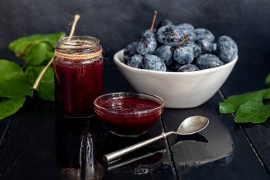 Kavanozda erik reçeli. Arka planda erikler var. Tkemali sosu. Kış için hazırlanıyorum. Koyu arkaplan.