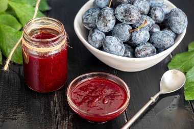 Kavanozda erik reçeli. Arka planda erikler var. Tkemali sosu. Kış için hazırlanıyorum. Koyu arkaplan.
