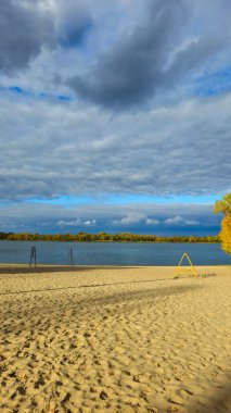 Ağaçlarda sarı yapraklar, yansımalar ve mavi gökyüzü olan sonbahar nehri manzarası. Şehir plajı. Bir sürü bulut. Turizm.