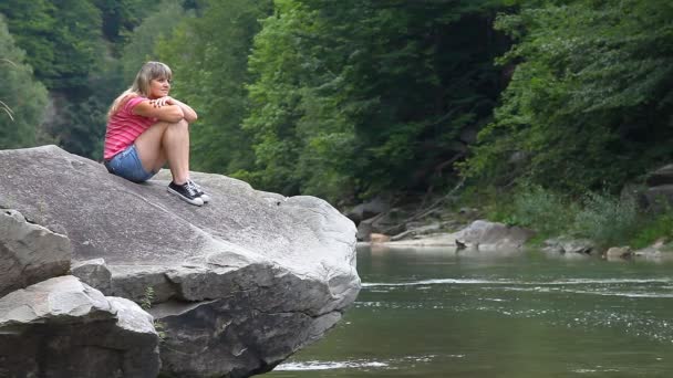 Mooi meisje zittend op de grote steen in de buurt van de rivier van de berg — Stockvideo