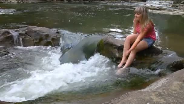 Joven chica hermosa se sienta en una piedra en un río de montaña — Vídeo de stock