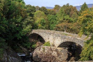 SCOTLAND, BÜYÜK BRITAIN - 12 Eylül. 2014: Bu, ormandaki bir çalılıktaki dağ deresinin üzerindeki eski bir kemerli taş köprü.