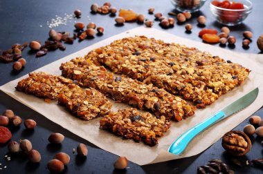 The concept of healthy delicious homemade dishes. Granola with nuts and dried fruits on a dark surface. Beside the ingredients for the preparation of granola, such as hazelnuts, walnuts, raisins and dried apricots
