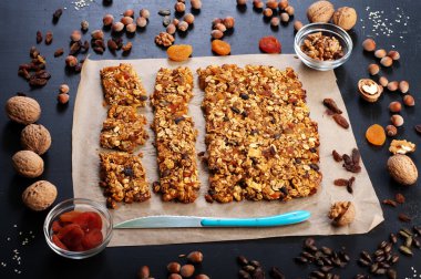 The concept of healthy delicious homemade dishes. Granola with nuts and dried fruits on a dark surface. Beside the ingredients for the preparation of granola, such as hazelnuts, walnuts, raisins and dried apricots
