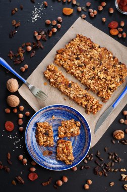 The concept of healthy delicious homemade dishes. Granola with nuts and dried fruits on a dark surface. Beside the ingredients for the preparation of granola, such as hazelnuts, walnuts, raisins and dried apricots