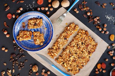 The concept of healthy delicious homemade dishes. Granola with nuts and dried fruits on a dark surface. Beside the ingredients for the preparation of granola, such as hazelnuts, walnuts, raisins and dried apricots