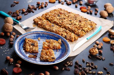 The concept of healthy delicious homemade dishes. Granola with nuts and dried fruits on a dark surface. Beside the ingredients for the preparation of granola, such as hazelnuts, walnuts, raisins and dried apricots