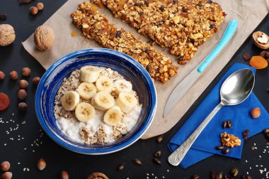 . Yulaf ezmesi, meyveler, kurutulmuş meyveler ve kuruyemişler ile koyu bir yüzeyde granola ve lezzetli kahvaltı. Fındık, ceviz, kuru üzüm ve kuru kayısı gibi granola hazırlanması için malzemeler yanında