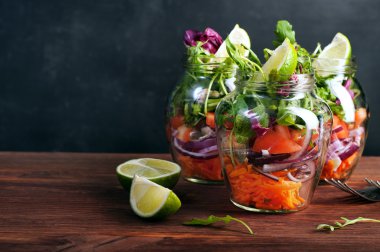 Salata arugula, havuç, domates, mor soğan ve limon ile cam bir kavanozda. Eğer bir cam kavanozda çalışmak için yanınıza alabilir sağlıklı gıda ev pişirme, kavramı. Vejetaryen salatası. Faydalı diyet yemeği.